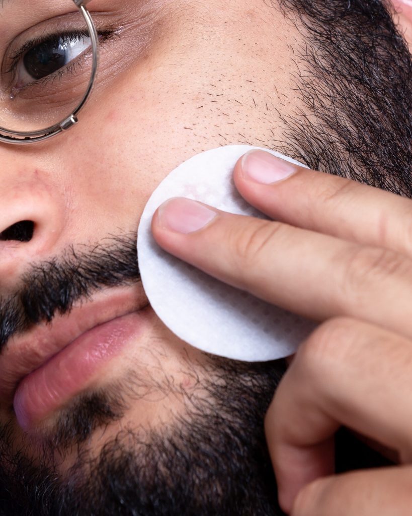 Homem com barba limpando o rosto com algodão