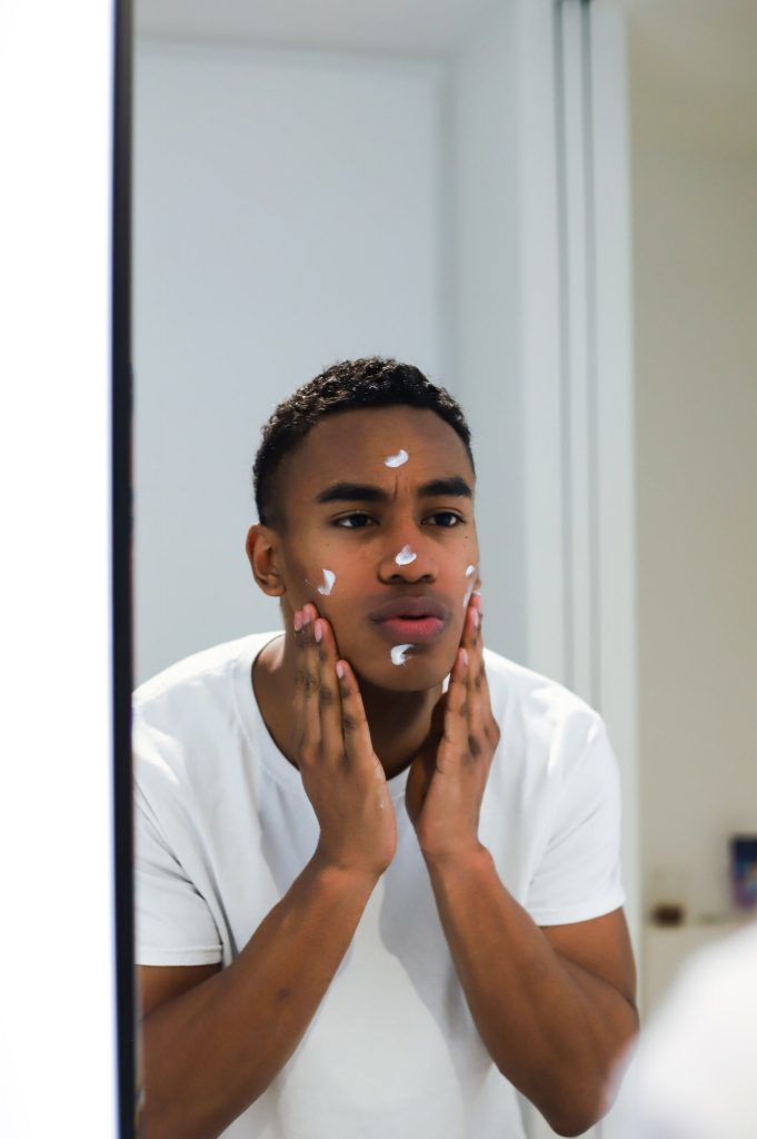 Homem negro olhando no espelho aplicando produto facial 