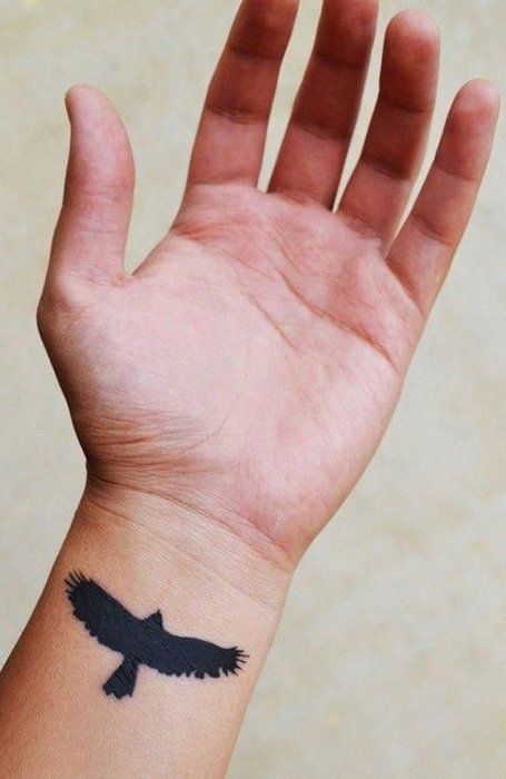 Tatuagem de silhueta de pássaro em pulso masculino