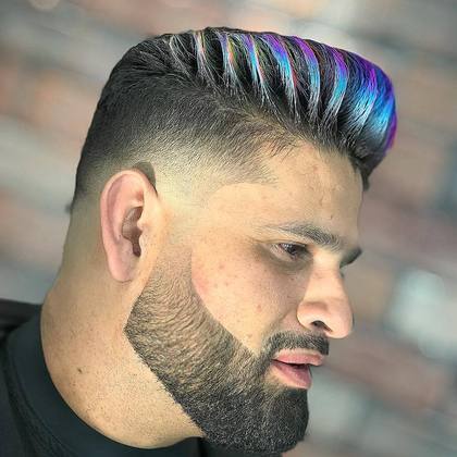 Perfil em close de homem branco, de barba em degradê, com corte blindado pintado de diferentes tons de azul indo até o roxo.