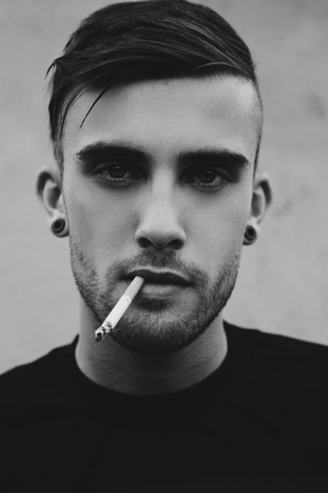 Imagem em preto e branco com close no rosto de rapaz fumando com um cabelo curto com undercut.