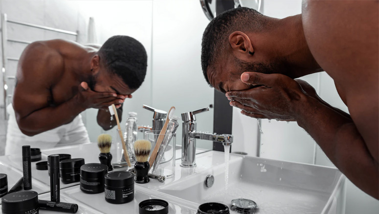 Homem negro lavando seu rosto em uma pia para evitar ter cravos e espinhas.
