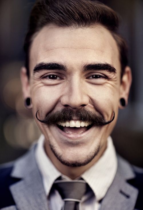 Homem branco sorridente com bigode estilo handlebar