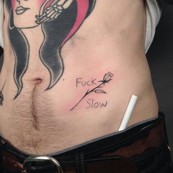 Close em tatuagem próxima a virilha com um rosa e os dizeres "fuck slow".