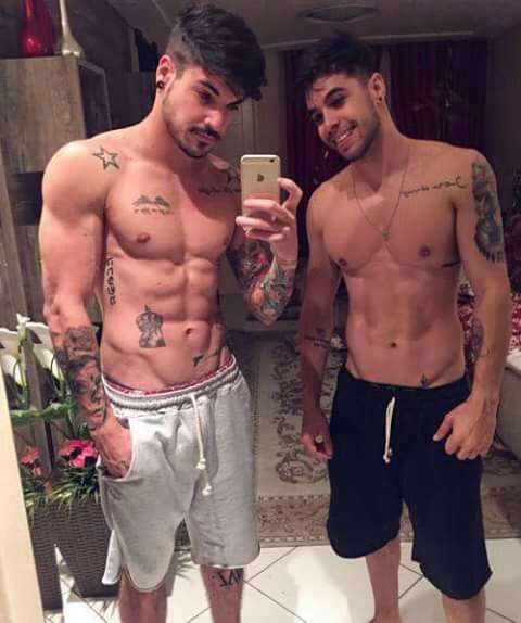 Dois rapazes sem camisa com a região próxima a virilha tatuadas.