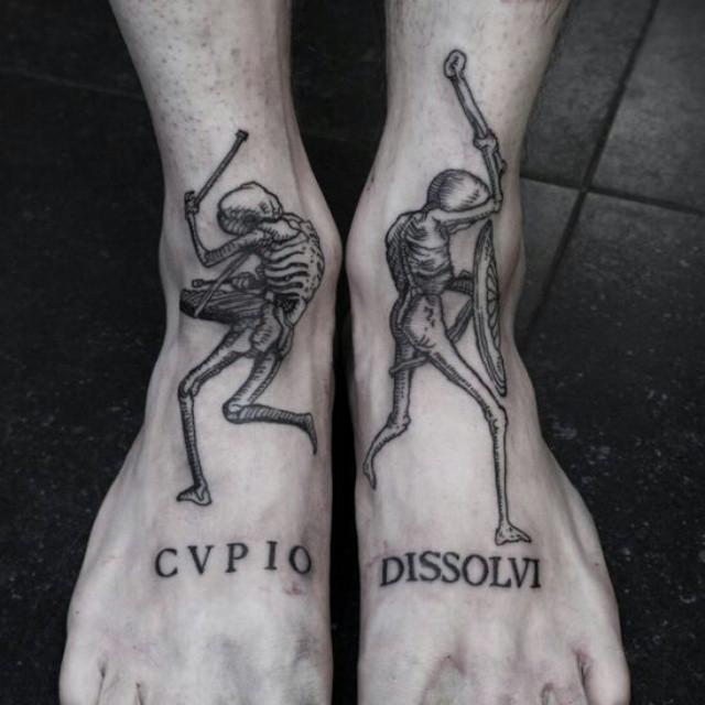 close em pé com tatuagens riscads com dois esqueletos soldados e com frases em latim em ambos os pés