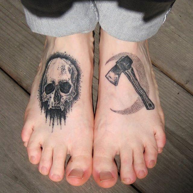 Close em pés com tatuagens pontilhadas, uma crânio e um machado a frente da lua minguante