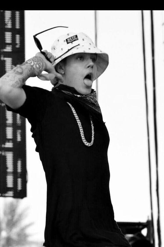 Justin Bieber de boca  aberta e m  um show  com  seu bucket hat estampado com pequenos logos.