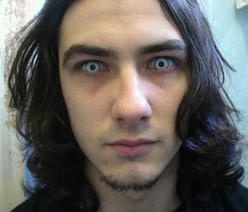 Rapaz branco com cabelos longos com lentes azul claro nos olhos.