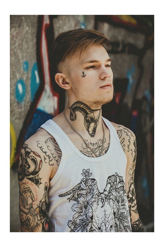 Rapaz branco, jovem, com tatuagem de ancora na lateral do rosto.