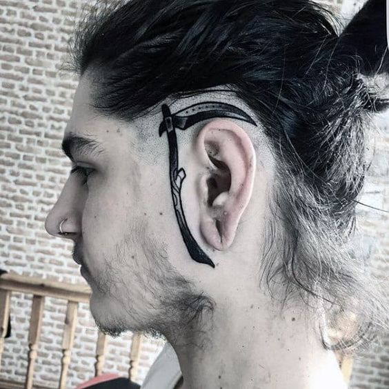 Close no rosto de um rapaz com uma tatuagem de foice na lateral de seu rosto.