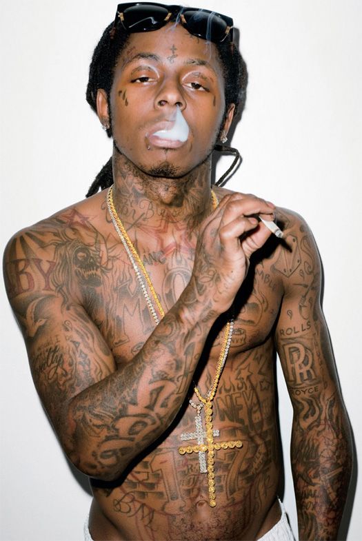Rapper Lil Wayne sem camisa, fumando um baseado exibindo suas tatuagens no rosto e no corpo.