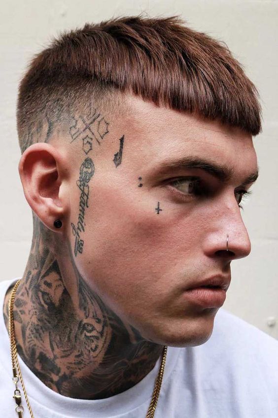 Rapaz branco com várias  pequenas tatuagens no rosto.