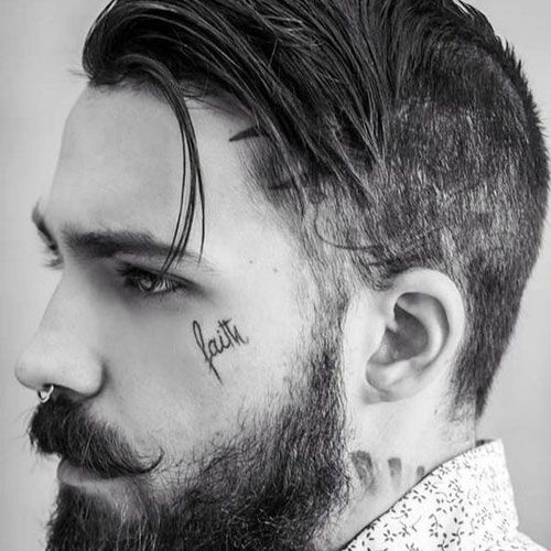 Perfil de um homem branco com close na tatuagem no rosto escrito 'faith'.
